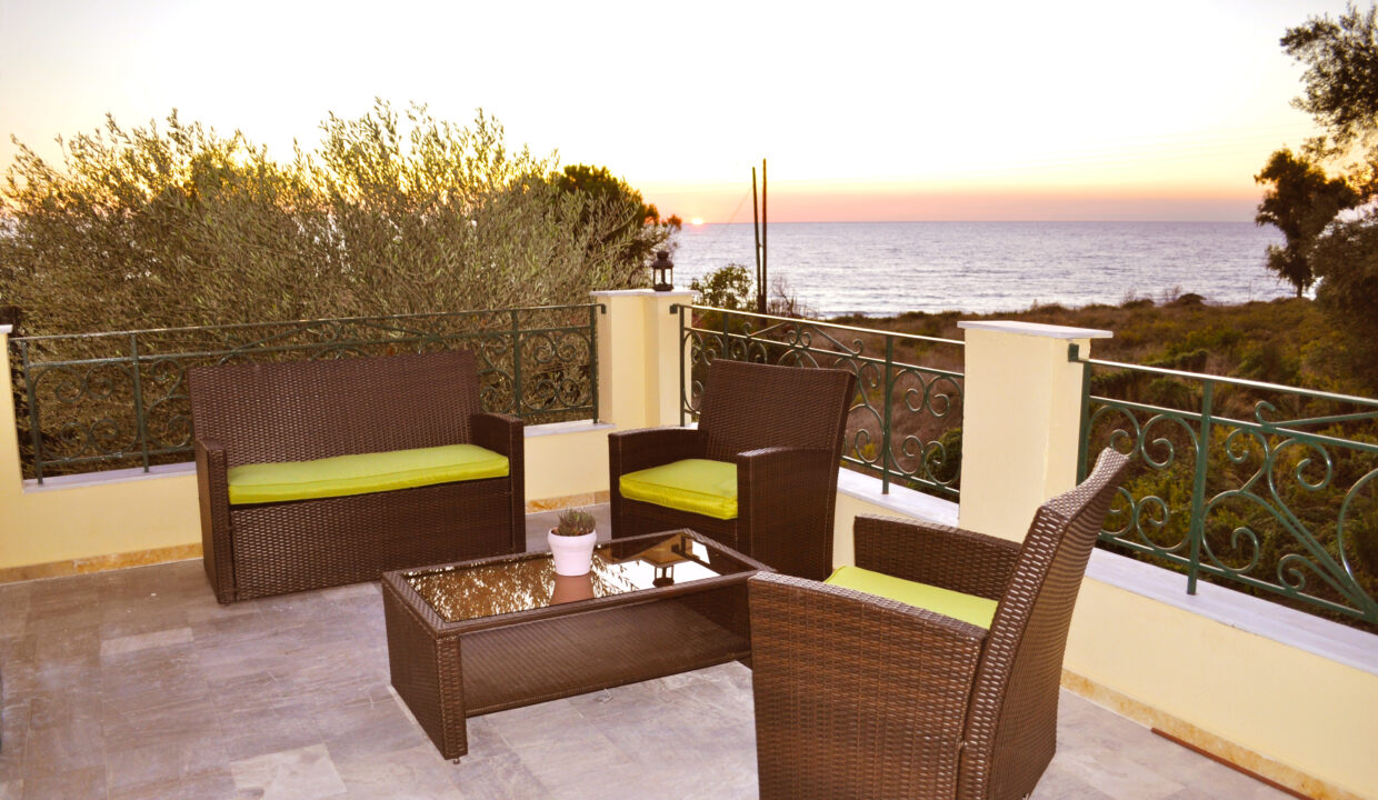 Ferienhaus Angelos C - überdachte Terrasse mit Gartenmöbeln und Blick aufs Meer.